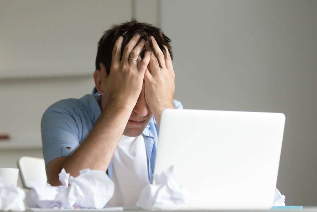 Portrait of man near laptop, his hands closing his face